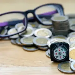 Okulary, stos monet i kompas symbolizują drogę do uzyskania dofinansowania do okularów.