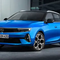 Błękitny Opel Astra Sports Tourer z czarnym dachem i felgami stoi przed nowoczesnym budynkiem.