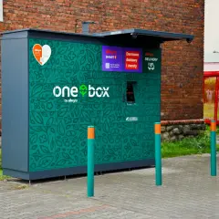 Zielony automat paczkowy Allegro One Box z motywem liści. Wymiary paczkomatu pozwalają na wygodne odbieranie i nadawanie przesyłek.