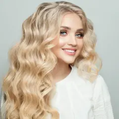 Mujer sonriente con cabello rubio mantequilla ondulado y ojos azules brillantes.