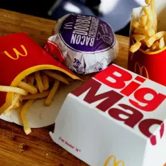Frytki z McDonald's w czerwonych opakowaniach obok pudełka Big Mac i burgera.