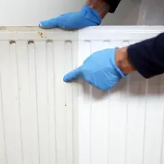 Manos enguantadas señalan un radiador a medio pintar, mostrando el antes y el después de pintar radiadores.