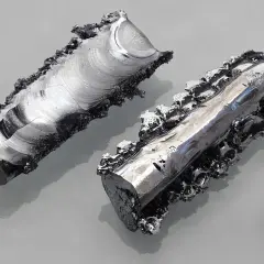 Zwei unregelmäßige Metallstücke mit glänzender, schillernder Chrom-Wirkung und ein kleiner Würfel daneben.