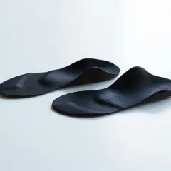 Zwei schwarze, ergonomisch geformte sensomotorische Schuheinlagen liegen auf weißem Untergrund.