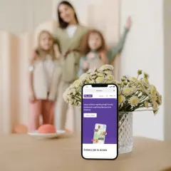 Telefon z aplikacją Bezpieczna Rodzina Play. Mama z dziećmi w tle. Zadbaj o bezpieczeństwo bliskich.