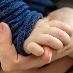 Eine Hand hält zart die kleine Hand eines Babys. Die Frage, warum hilft Gott nicht bei Depressionen, hallt in dieser Geste der Verbundenheit wider.