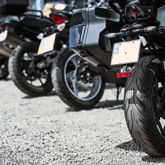 Varias motos aparcadas en fila, una moto sin matrícula visible en primer plano, con su rueda trasera y maleta.