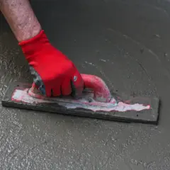 Ręka w czerwnej rękawicy wygładza mokrą wylewkę samopoziomującą do garażu za pomocą kielni.