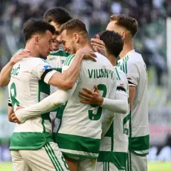 Piłkarze z Gdańska w białych strojach z zielonymi pasami świętują razem na boisku.