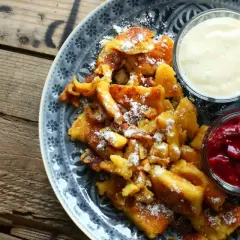Ein köstlicher Kaiserschmarrn, bestäubt mit Puderzucker, serviert mit Apfelmus und Vanillesauce. Ein einfaches Rezept für Genuss.