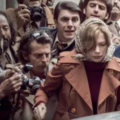 Otoczona przez paparazzi, kobieta w brązowym płaszczu i mężczyzna w okularach wyglądają, jakby chcieli zdobyć wszystkie pieniądze świata, by uciec od tej uwagi.