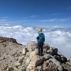 Widok z góry na chmury, osoba z plecakiem i kijkami trekkingowymi na skalistym szczycie. To wspaniałe wejście na Teide!