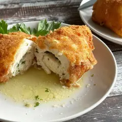 Złocisty kotlet de volaille, przekrojony na pół, odsłaniający soczyste wnętrze z ziołami, pływa w maśle.