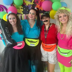 Cuatro amigas celebran una fiesta moda de los 80 con atuendos coloridos, riñoneras y peinados voluminosos.
