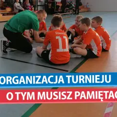 Trener w zielonej koszulce tłumaczy dzieciom w pomarańczowych strojach, jak zorganizować turniej piłki nożnej.