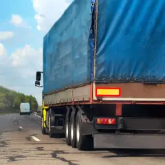 Ciężarówka z niebieską plandeką jedzie drogą. Kierowca uważa na zakaz jazdy na Węgrzech, by uniknąć kary.