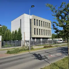 Nowoczesny dom wielorodzinny w budowie, obok elegancka willa, ulica i drzewa.