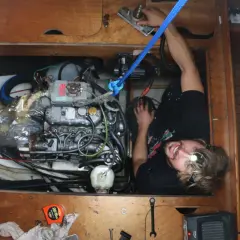 Uomo con torcia frontale lavora sul motore di una barca, tra tubi e cavi. Il calcolo carburante nautica è fondamentale per la navigazione.
