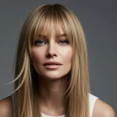Blonde Frau mit Curtain Bangs, die ihr Gesicht umrahmen. Ihr Blick ist direkt in die Kamera gerichtet.