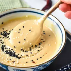 A creamy tahini dressing, sprinkled with black and white sesame seeds, is scooped from a bowl. This tahini sauce is a delicious alternative to miso for many dishes.