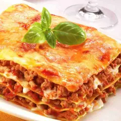 Porzione di lasagne fatte in casa, stratificate con ragù e besciamella, guarnite con basilico fresco.