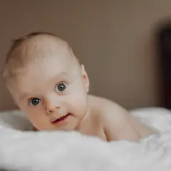 Niemowlę z niebieskimi oczami leży na białym kocyku. Jego wzrok jest skupiony, a usta lekko rozchylone. Zez u niemowlaka jest widoczny, ale nie przeszkadza mu w eksplorowaniu świata.