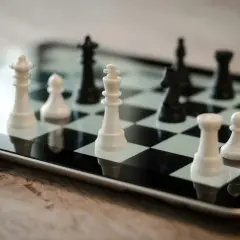 Białe i czarne figury szachowe na ekranie tabletu. Król i pionki białych na pierwszym planie, czarne figury w tle. Gra w szachy na różnych poziomach.