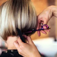 Fryzjerka precyzyjnie modeluje prosty bob, używając kolorowych nożyczek.