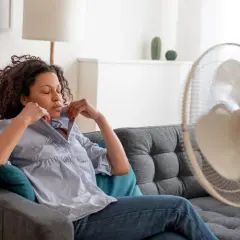 Frau in 40. SSW kämpft mit Hitzewallungen, versucht sich mit einem Ventilator Linderung zu verschaffen.