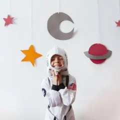 Uśmiechnięte dziecko w stroju astronauty na tle kosmicznych dekoracji.