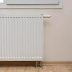 Biały grzejnik pod oknem, termostat ustawiony na 60 stopni, ale grzejniki letnie.