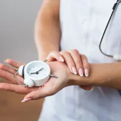 Manos de profesional de la salud sostienen un reloj despertador, simbolizando la presión de trabajo y la importancia del tiempo en la atención médica.