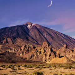 Krajobraz księżycowy z widocznym w oddali masywem wulkanicznym. Wczesny wieczór, na niebie sierp księżyca. Wejście na Teide.
