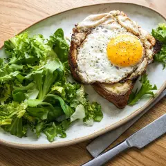 Ein herzhafter Croque Madame mit Spiegelei, Käse und Toast, serviert mit frischem Salat.