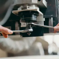 Dwie ręce dokręcają kluczem element wrzeciona maszyny CNC, precyzyjnie ustawiając go zgodnie z wzorem na prędkość skrawania.