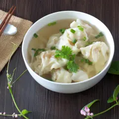 Aromaticzne chińskie pierożki w bulionie, ozdobione szczypiorkiem i kolendrą, gotowe do spożycia z pałeczkami.
