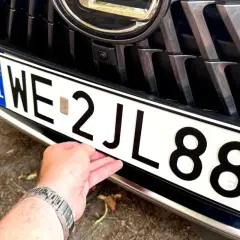 Dłoń poprawia tablicę rejestracyjną z numerem WE 2JL88, przygotowując wniosek o rejestrację pojazdu.