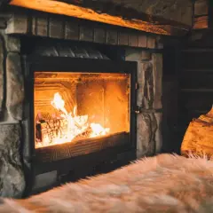 Un feu crépite joyeusement dans une cheminée en pierre, réchauffant l'atmosphère d'un chalet rustique. Des bûches attendent patiemment à côté.