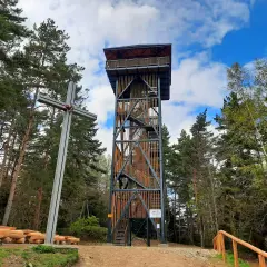 Skiełek wieża widokowa w otoczeniu lasu, obok metalowy krzyż i drewniane ławki.