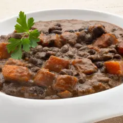 Un plato de frijoles negros con trozos de camote y perejil fresco.