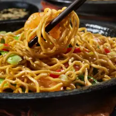 Un plato humeante de fideos con pollo, salteado con verduras y semillas de sésamo, listo para ser disfrutado.