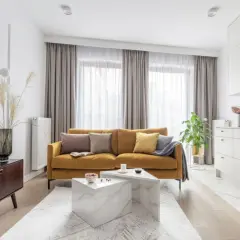 Musztardowa kanapa inspiracje: przytulny salon z nowoczesną kuchnią. Miękkie poduszki i pled dodają ciepła.