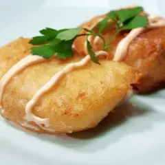 Dos trozos de bacalao rebozado, dorados y crujientes, servidos con una salsa cremosa y perejil fresco.