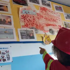 Niña con casco de bombero señala un mural de bomberos, parte de originales proyectos infantiles.