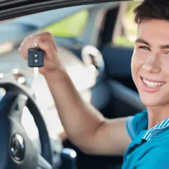 Uśmiechnięty młody mężczyzna trzyma kluczyki do swojego pierwszego auta. Idealne jakie auto na pierwsze!