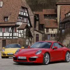 Dwa Porsche, czerwone i żółte, stoją przed zabytkowymi domami. Czy to PDK?