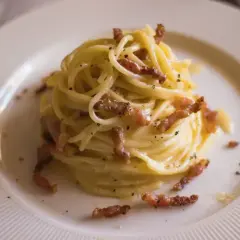 Pyszne spaghetti carbonara z chrupiącym guanciale, kremowym sosem i czarnym pieprzem na białym talerzu.