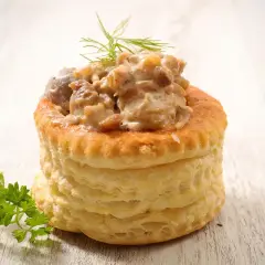 Une délicieuse bouchée à la reine, garnie d'une sauce crémeuse aux champignons et volaille, sur fond de bois clair.