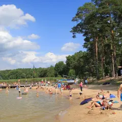 Słoneczny dzień nad jeziorem w Augustowie. Ludzie kąpią się, opalają na plaży i spacerują po molo.