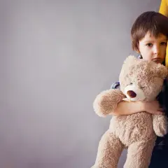 Smutne dziecko płacze, tuląc misia, gdy mama wychodzi.